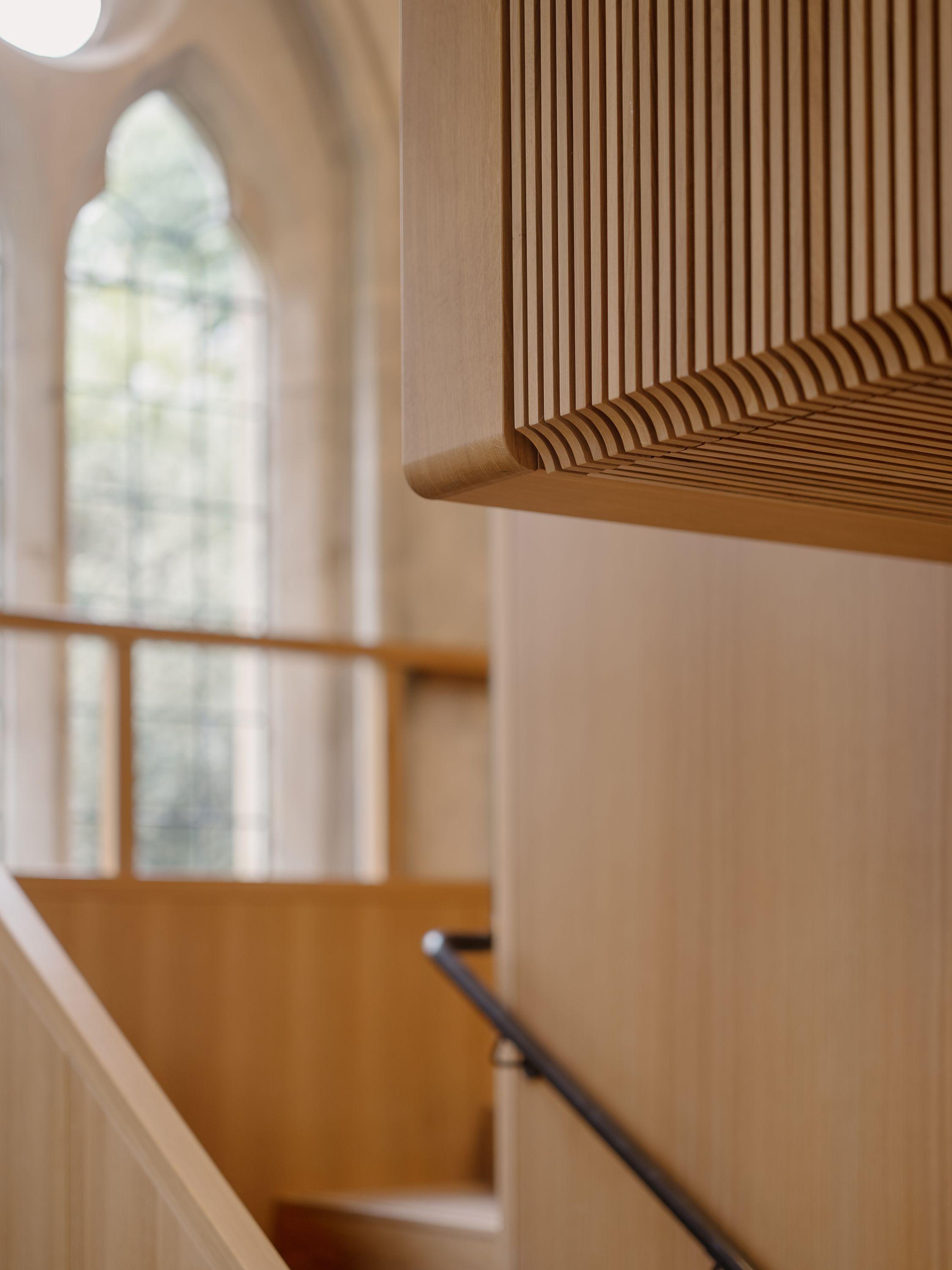 Detail of the oak-lined balcony at Exeter College Library, Oxford, its slatted timber soffit meeting a restored full-height gothic window with the garden beyond