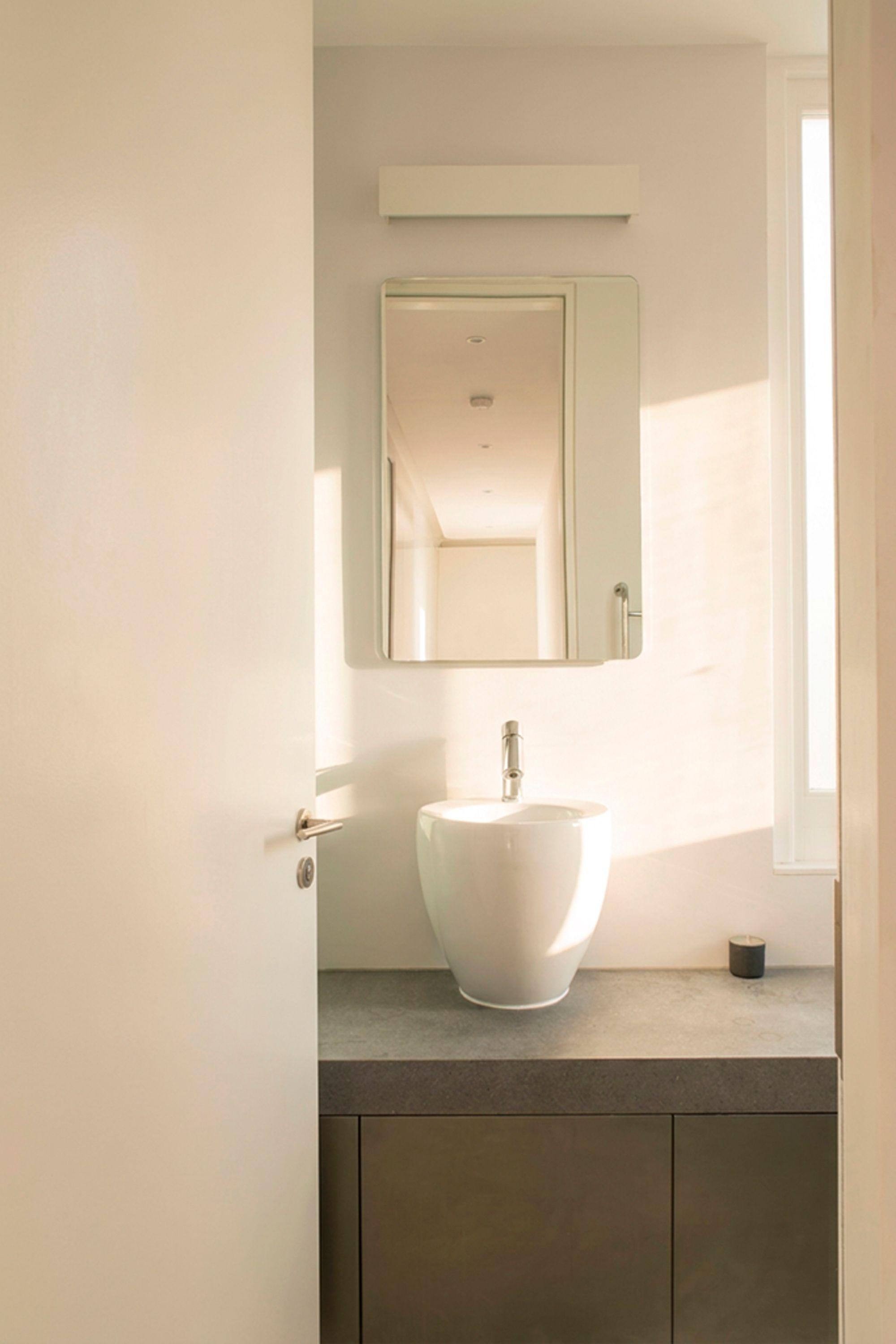 A bathroom in a refurbished apartment, light on a white basin above a stone counter and dark timber vanity
