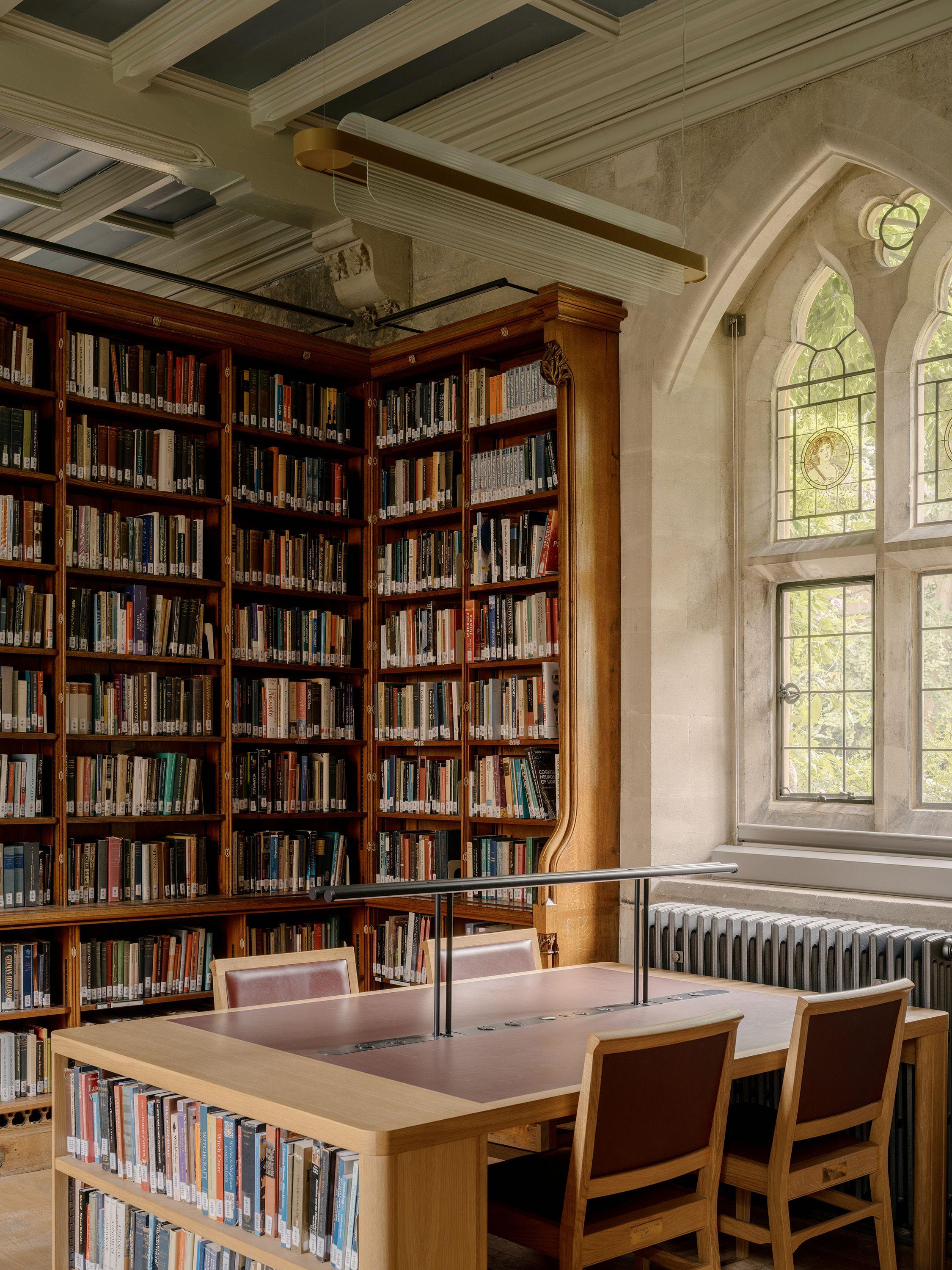 Study desk with under-desk book storage and integrated lighting at Exeter College Library, Oxford, beneath Scott's revealed ceiling and a restored window.