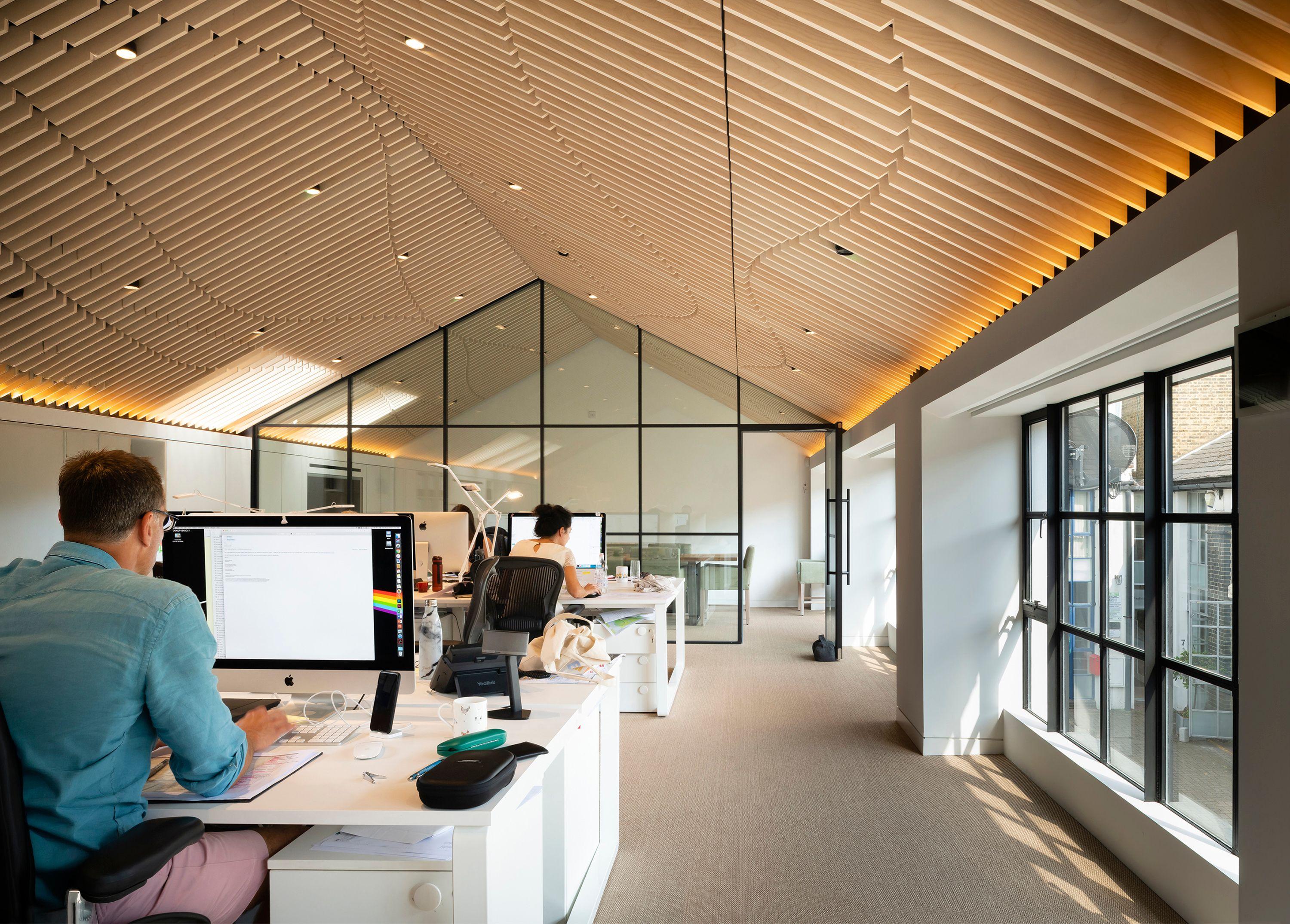 Interior of the Fluid Workspace, staff at long shared desks beneath a pitched timber-battened ceiling with a glazed gable partition behind.