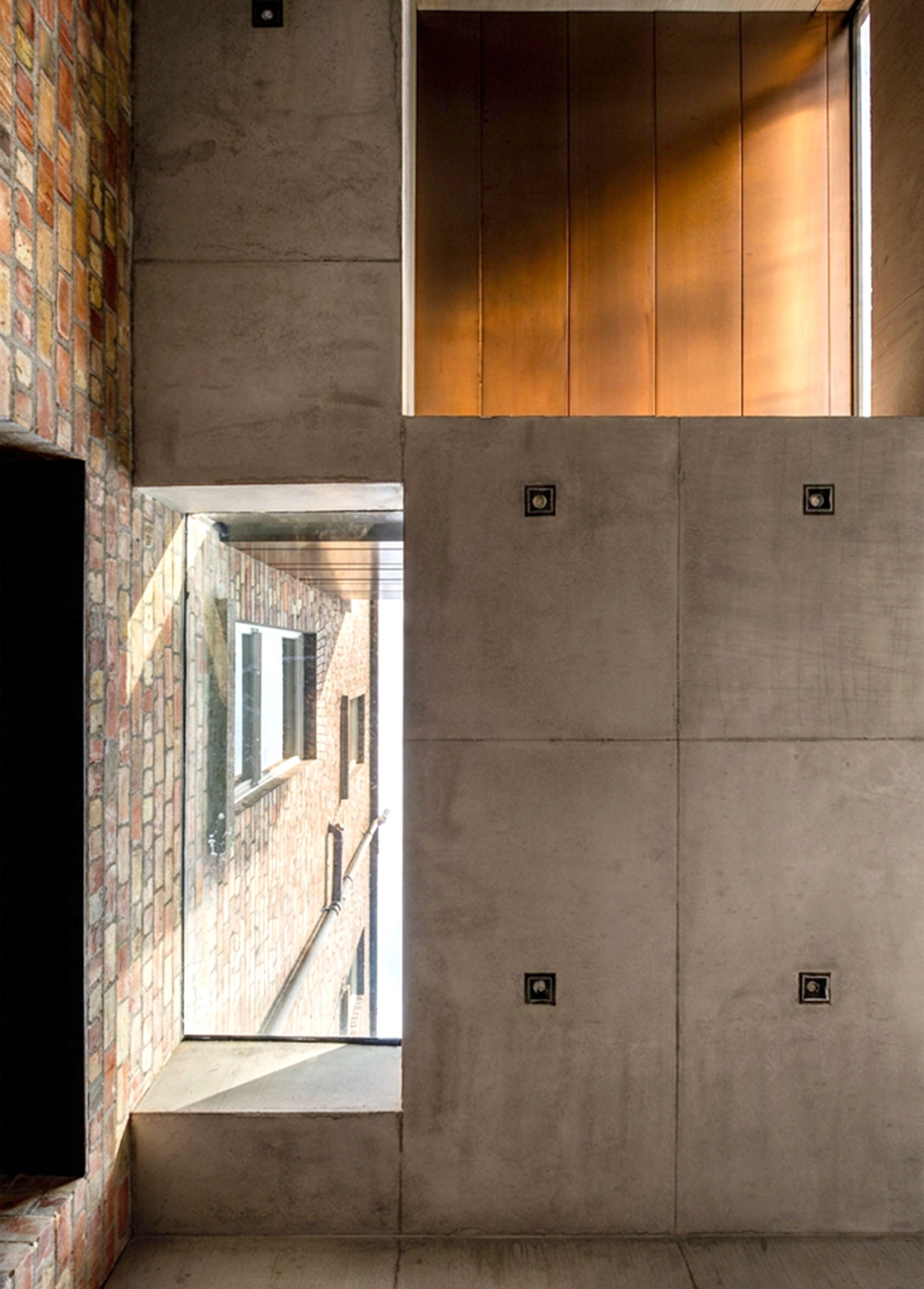 Junction at Half Landings House where the concrete extension meets the original brick wall, a bronze soffit overhead marking the bedroom above.