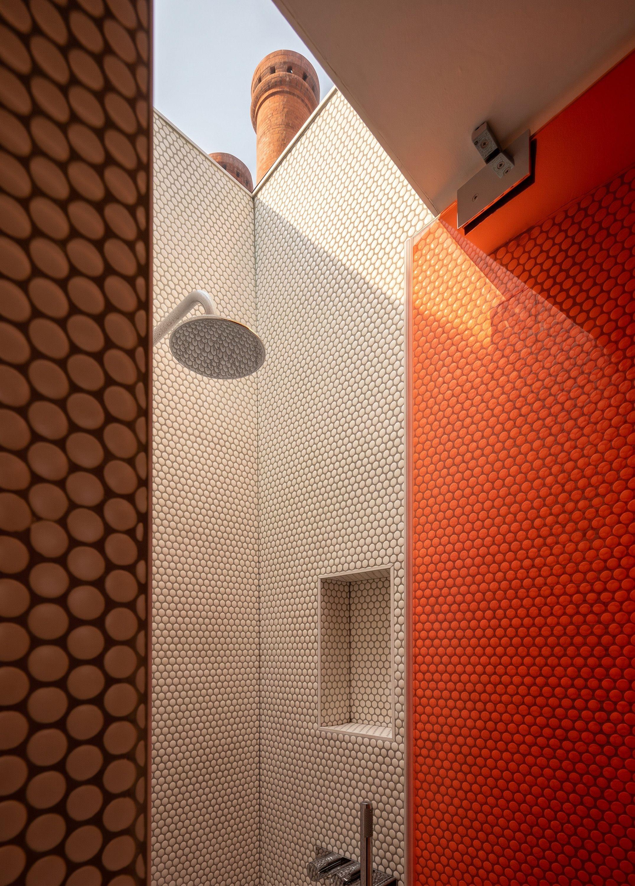 Rooflit shower at Puzzle Box lined in penny round tiles of brown, white and orange, a brick chimney visible through the skylight above