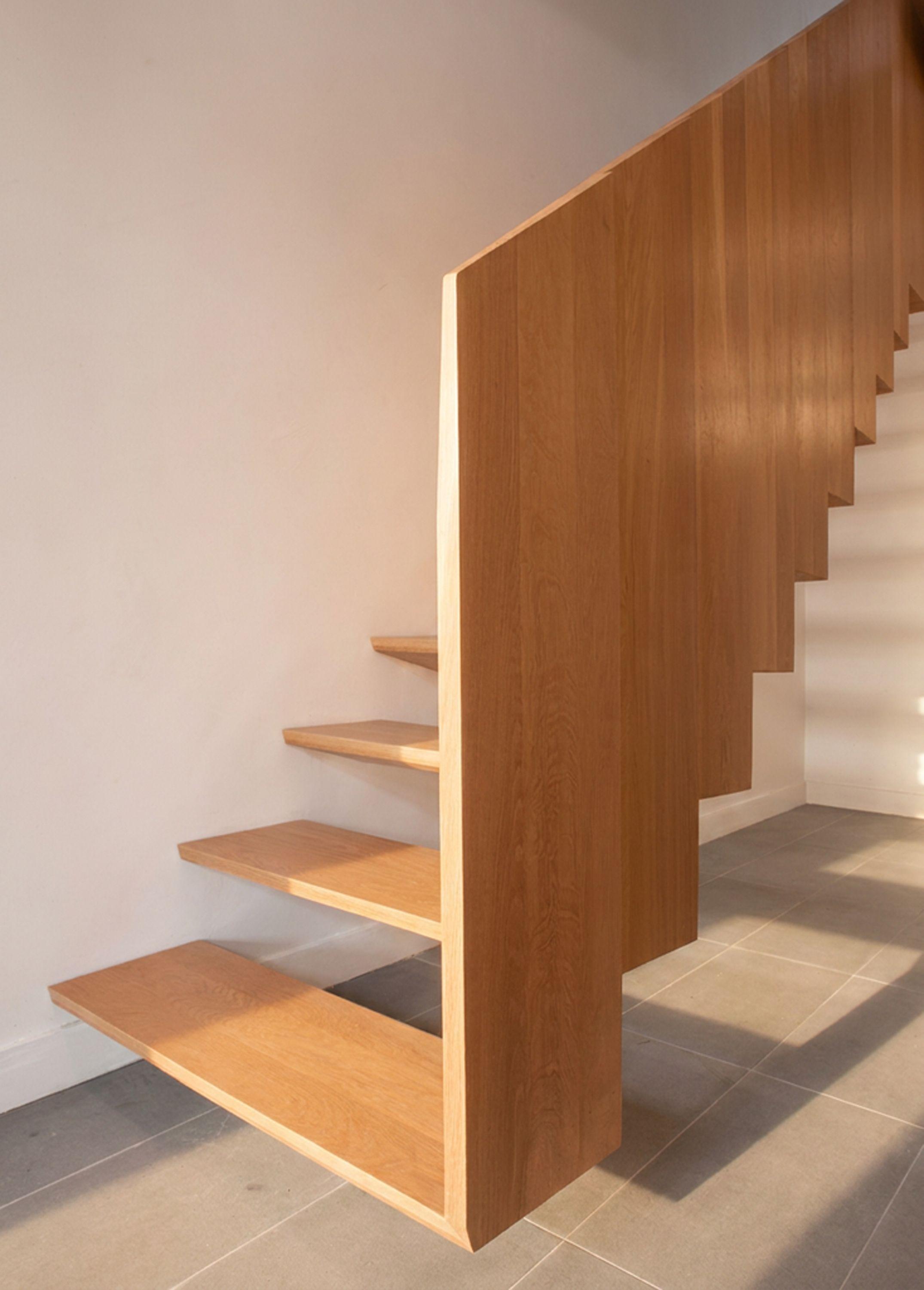 Foot of the new oak stair at Half Landings House, treads cantilevering from a solid timber balustrade above a tiled floor.