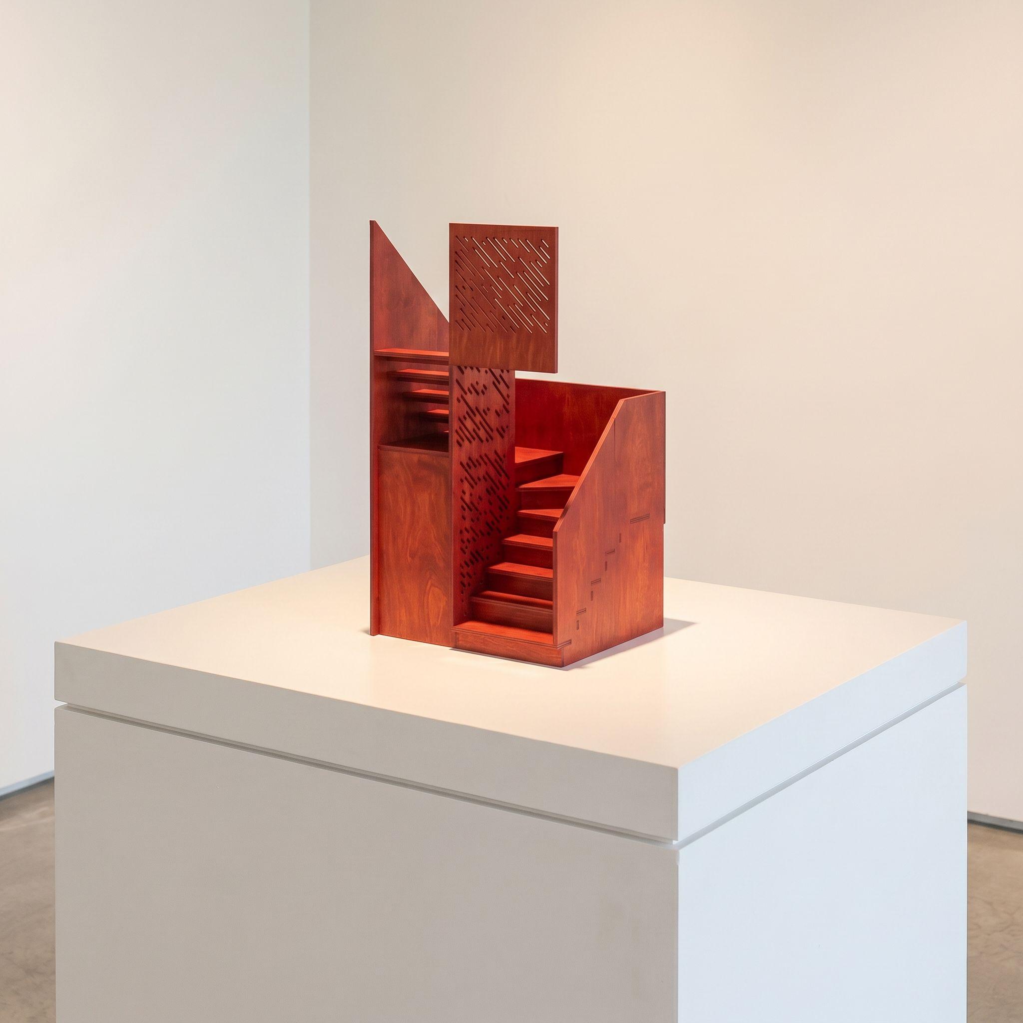 Scale model of the Cross Cut House stair, its red plywood form displayed on a gallery plinth, revealing the steps and cut balustrade pattern.