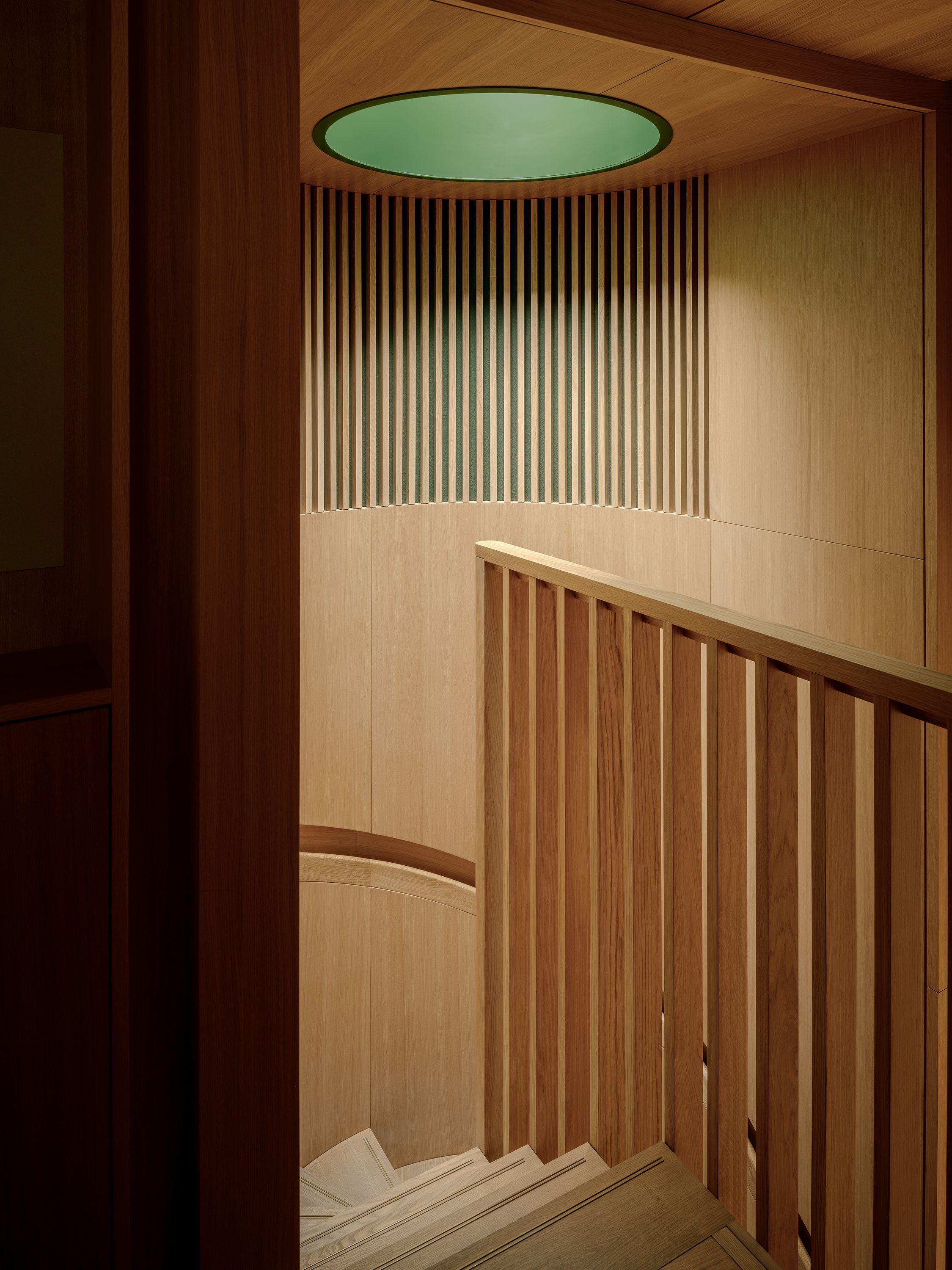 The new stair in the Link block at Exeter College Library, Oxford, lined in oak with a slatted balustrade and green light falling from the circular rooflight above.