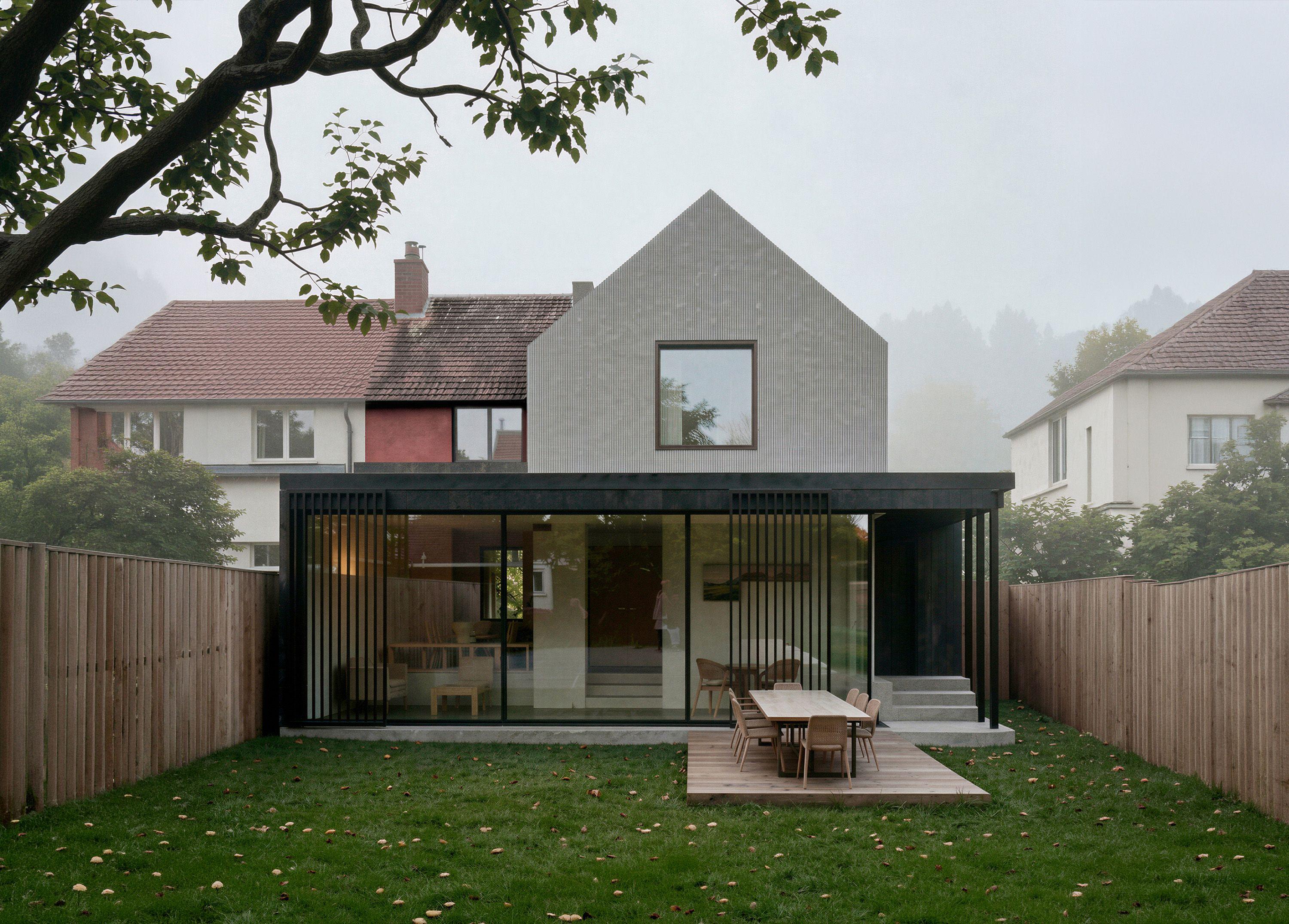 Garden elevation of the Hills Avenue house, Cambridge, with the glazed extension and timber louvres below and the fluted fibre cement gable above, seen from the lawn in morning mist.