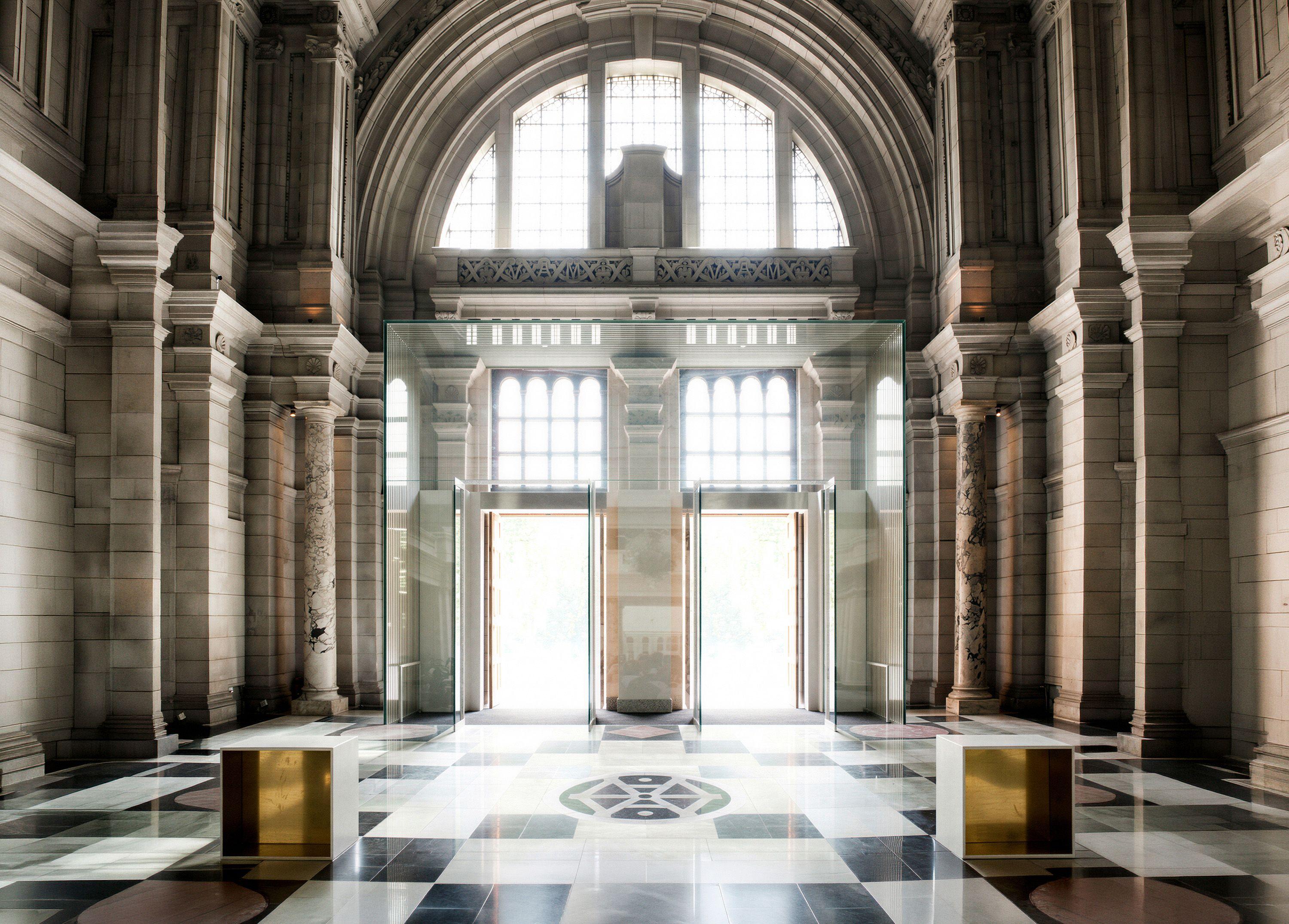 Visualisation of the proposed V&A Museum entrance, London, a tall glass gateway standing within Aston Webb's historic hall, its doors open to daylight beyond.