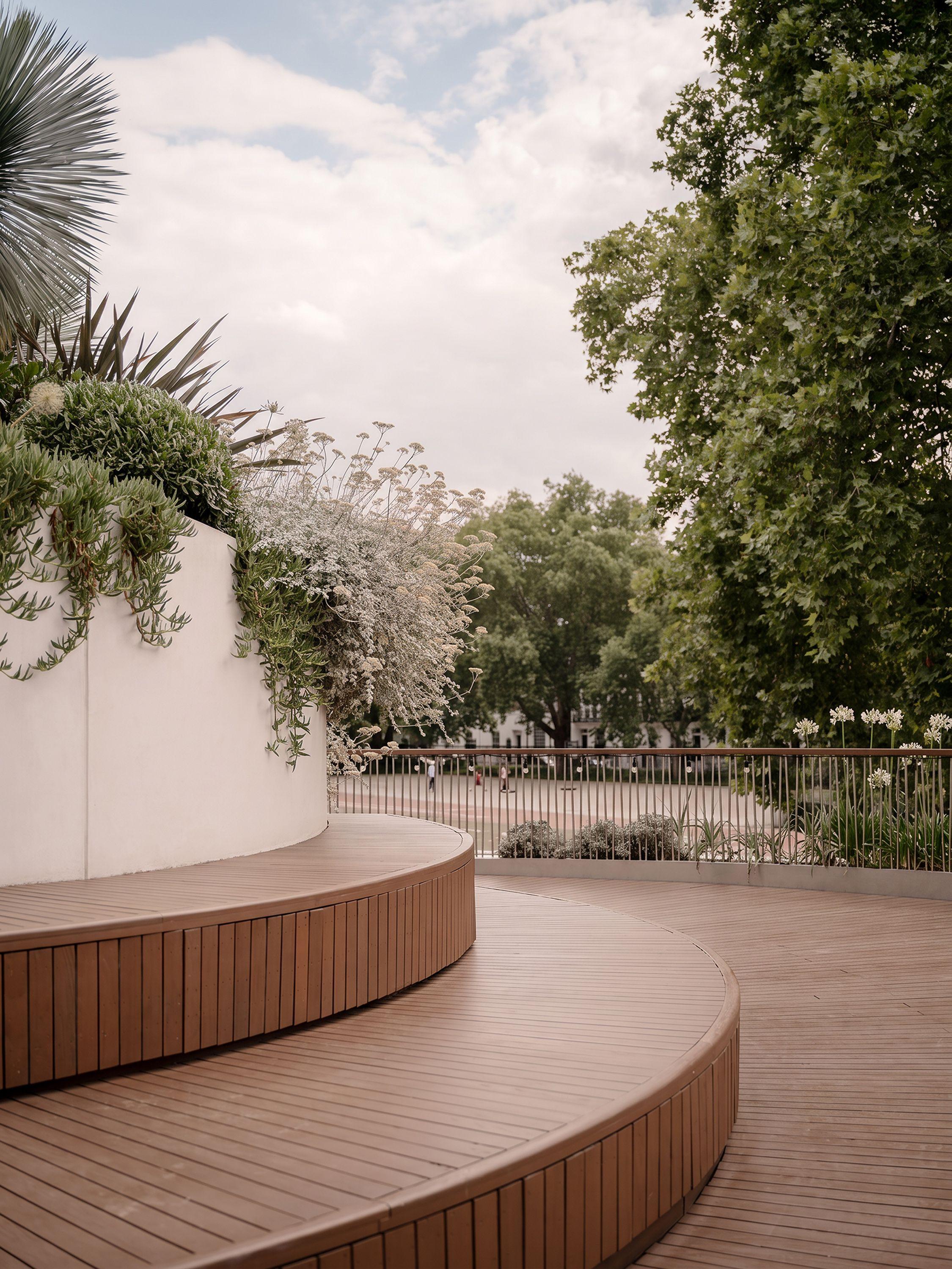 The public roof garden at Vardo, Duke of York Square, London, its curved timber deck and stepped seating following the spiral of the building, with planting and the treetops of the square beyond.